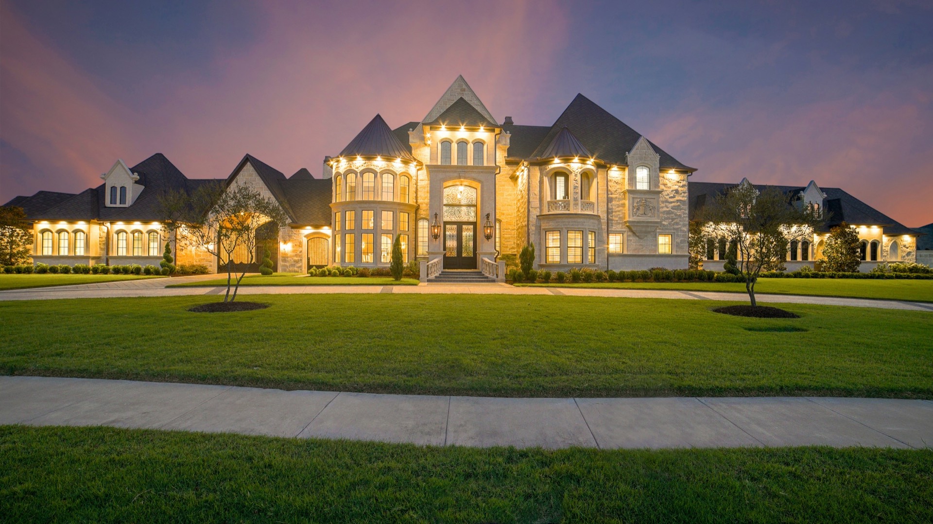 Contemporary white and black concrete house illuminated at dusk, viewed from the front drive — luxury property at golden hour